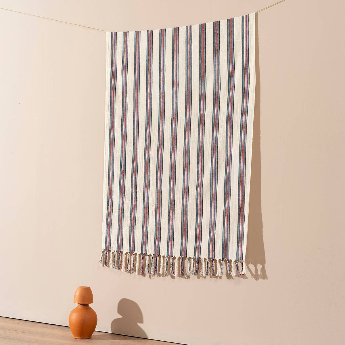Rose and navy pinstripe Turkish beach towel hung against a warm wall | Kikoya