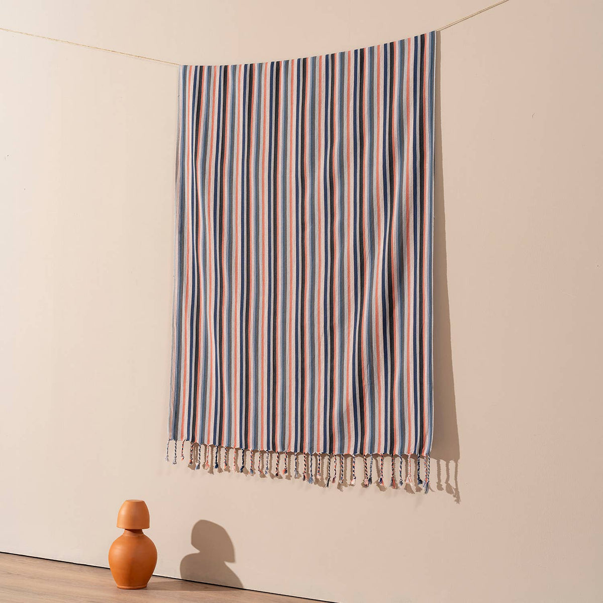 Terracotta and blue stripe Turkish beach towel hung against a warm wall | Kikoya