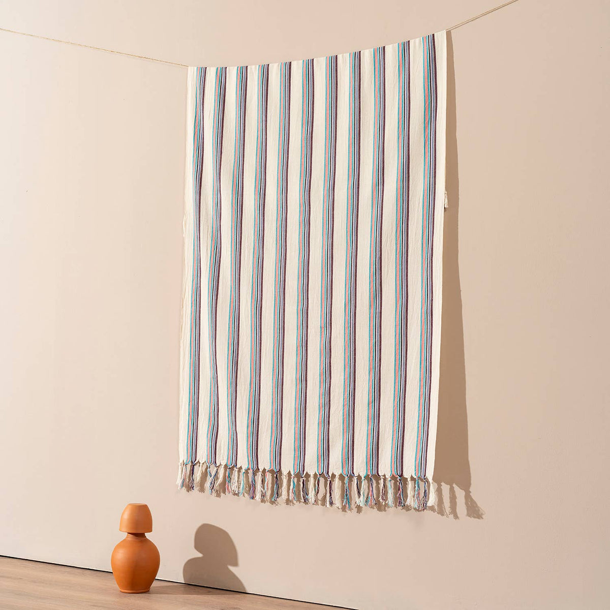 Teal and plum pinstripe Turkish beach towel hung against a warm wall | Kikoya
